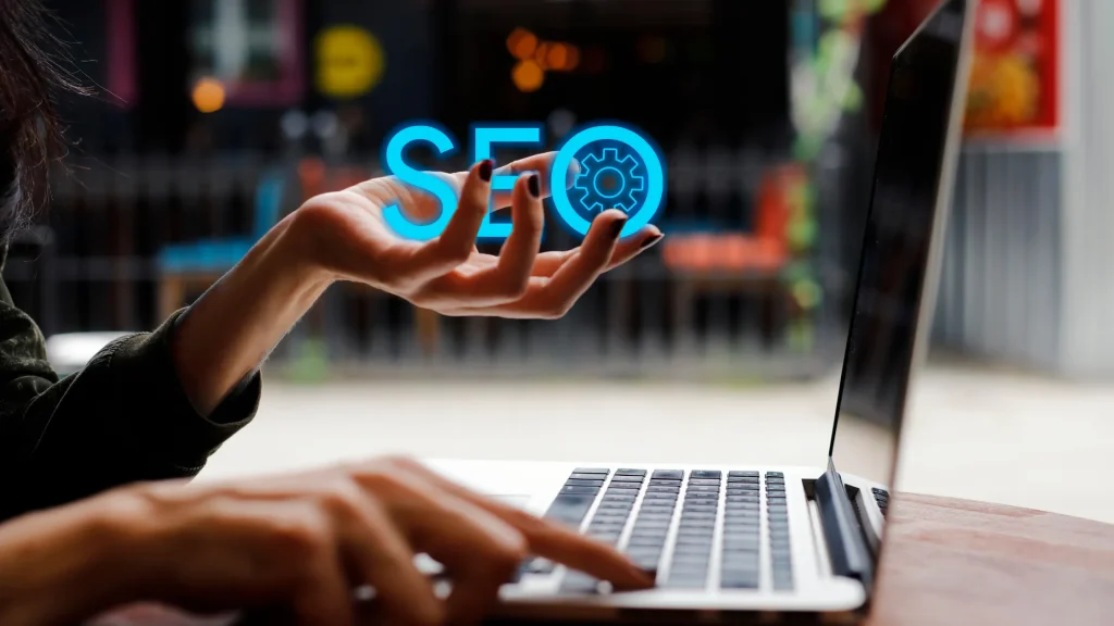 Hand holding SEO icon near a laptop, highlighting the importance of SEO for Bankruptcy Lawyers in digital client acquisition.